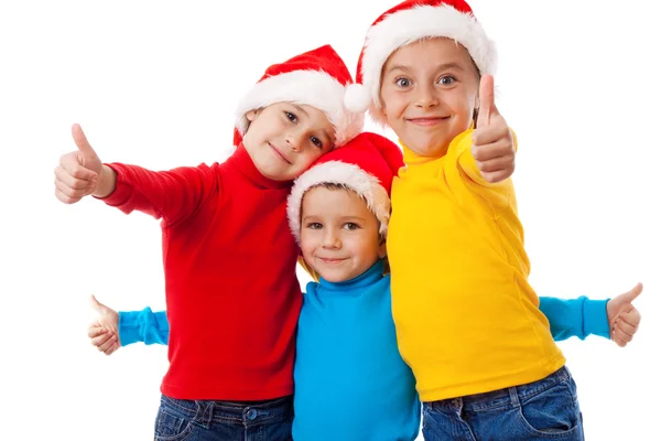 Трое улыбающихся детей в шляпах Санты с большим пальцем вверх вывеской — стоковое фото