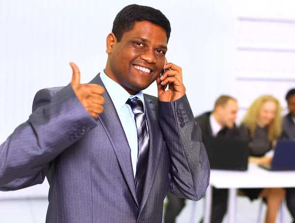 Αφρο-αμερικανικό επιχειρηματίας, μιλώντας στο κινητό τηλέφωνο με την ομάδα του στην πλάτη — Φωτογραφία Αρχείου
