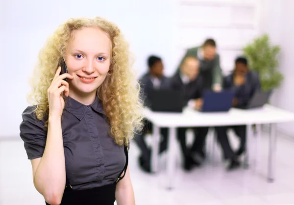 Close-up de bela jovem mulher falando no telefone celular com a equipe em backgr — Fotografia de Stock
