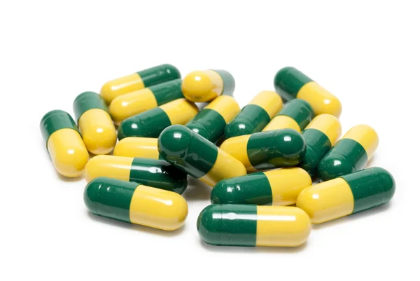 Zelená žlutá kapsle léky jsou roztroušeny na stůl — Stock fotografie