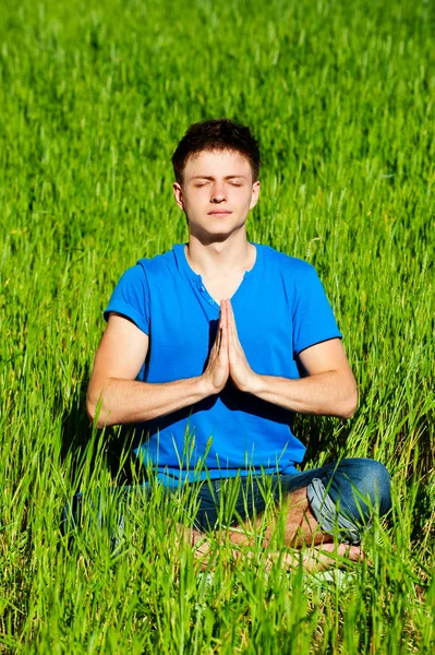 Молодой человек медитирует на зеленой траве — стоковое фото
