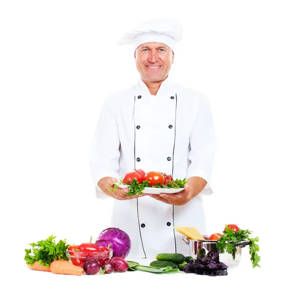 Happy chef holding plate with fresh vegetables — Stock Photo, Image