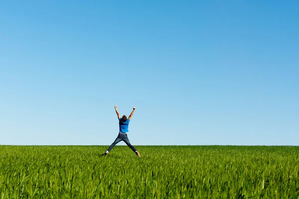Hombre saltando en el campo verde sobre el cielo azul —  Fotos de Stock