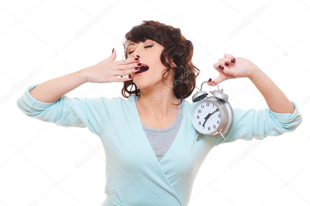 Woman holding alarm clock and yawning
