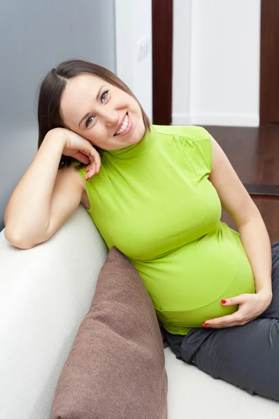 怀孕的女人抱着她的肚子和坐在沙发上 — 图库照片