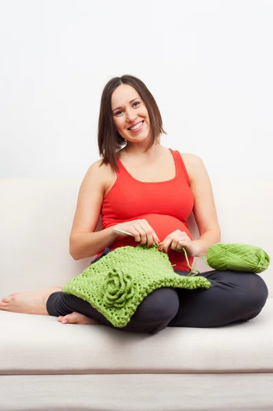 Pregnant woman sitting on sofa and crocheting — Stock Photo, Image