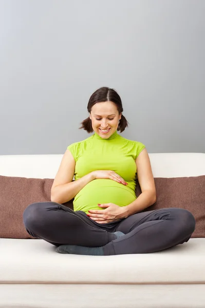 Έγκυος γυναίκα σε πράσινο μπλουζάκι που κάθεται στον καναπέ — Φωτογραφία Αρχείου