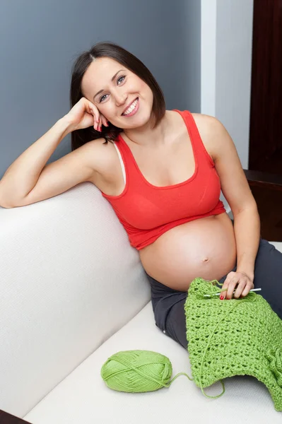 Mulher grávida sentada no sofá e segurando crochê — Fotografia de Stock