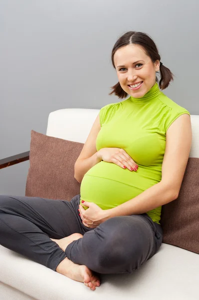 Smiley έγκυος γυναίκα που κάθεται στον καναπέ — Φωτογραφία Αρχείου