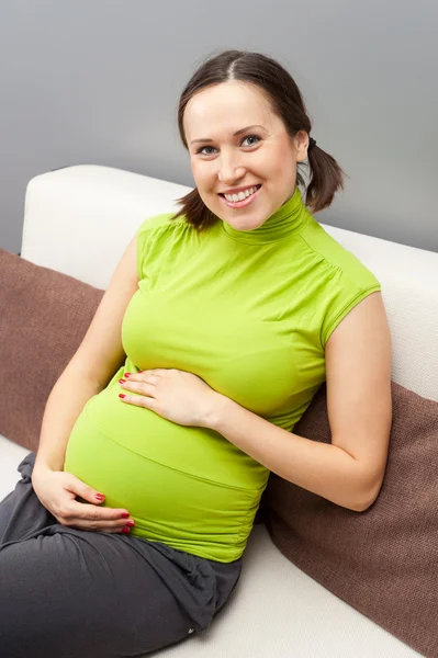 Gravid kvinna som sitter på soffan Royaltyfria Stockfoton
