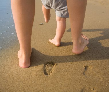 Anne ve çocuk bir kumsalda yürüyen