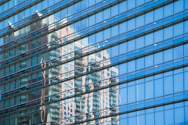 Cropped section of high rise office block with blue windows and reflection of another building in the windows.