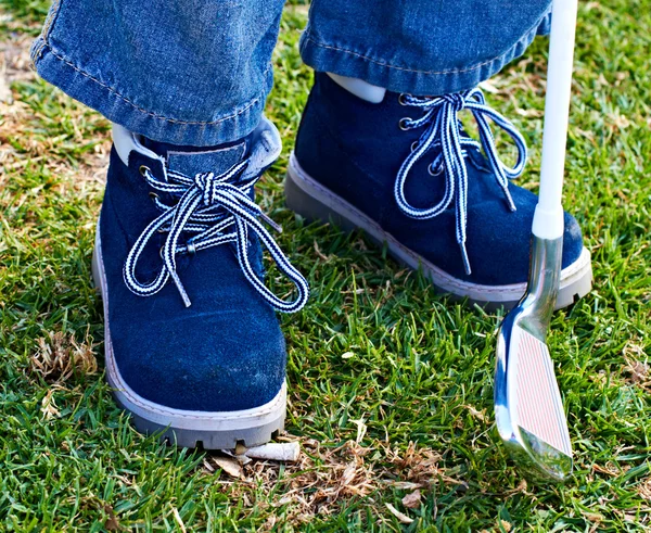 Anak laki-laki sepatu dan klub golf di rumput — Stok Foto