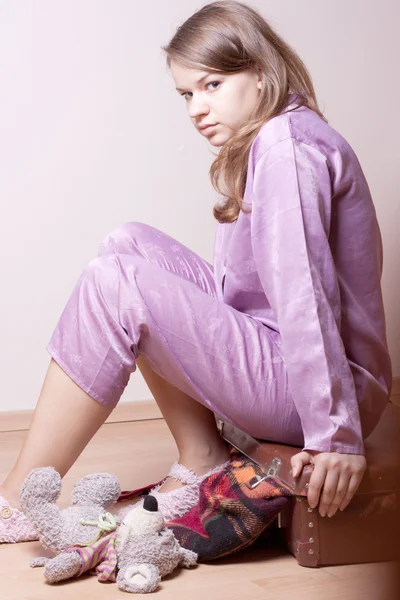Das Mädchen im lila Pyjama auf einem Koffer sitzend — Stockfoto