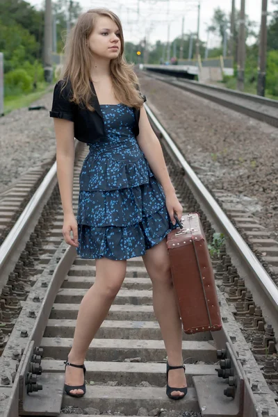 Chica con una maleta de pie sobre los rieles —  Fotos de Stock