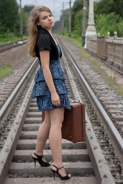 Girl with a suitcase standing on the rails — Zdjęcie stockowe