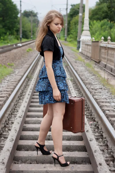 Chica con una maleta de pie sobre los rieles — Foto de Stock