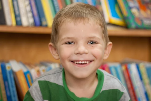 Маленький мальчик улыбается на фоне книг — стоковое фото