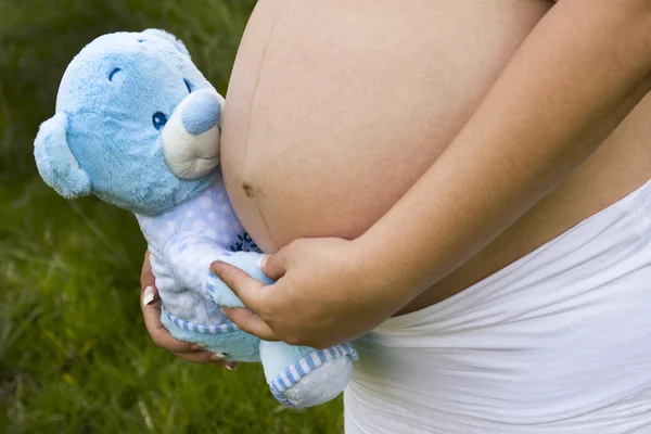 Pregnant woman holding a blue bear next to her tummy — Stock Photo, Image