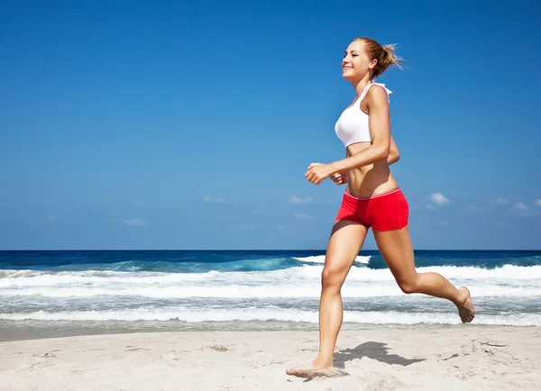 Gesunde Frau läuft am Strand Stockfoto