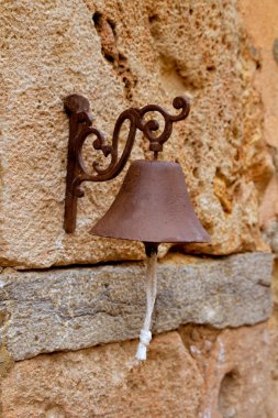 Aged rusty iron little bell hanging from stone wall clipart