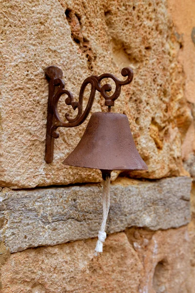 Старий іржавий залізний маленький дзвін, що звисає з кам'яної стіни — стокове фото