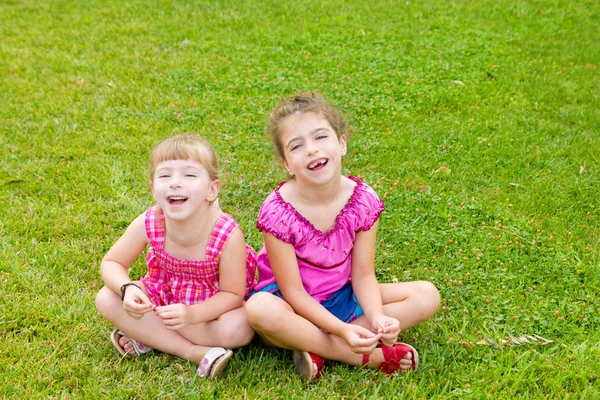 Дитячі дівчата сміються сидять на зеленій траві — стокове фото