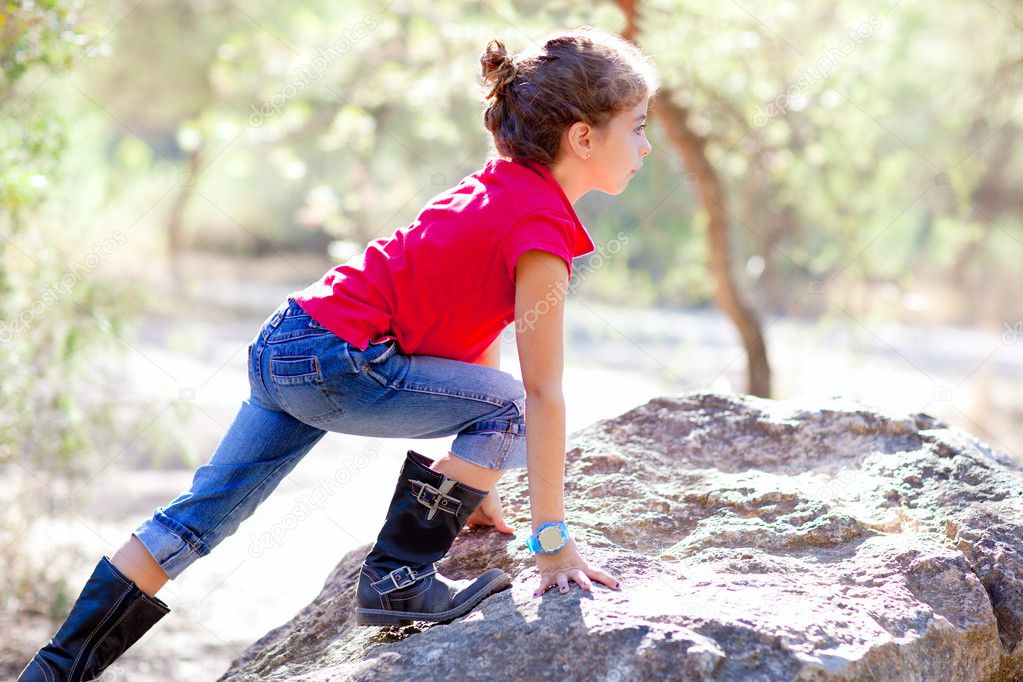 Hiking little girl climbing a rock in forest