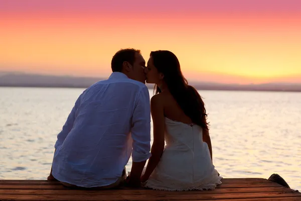 Couple embrasser au coucher du soleil assis dans jetée Images De Stock Libres De Droits