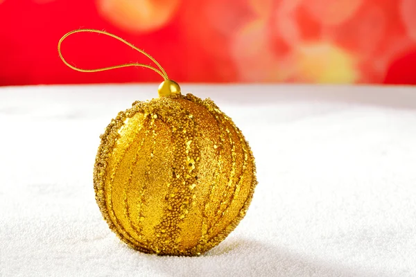 Рождественская золотая безделушка на снегу и красном — стоковое фото