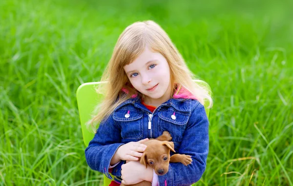 Sarışın çocuk kızla yeşil çim içinde evde beslenen hayvan köpek yavrusu — Stok fotoğraf