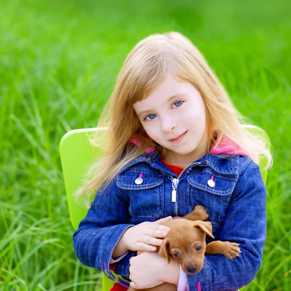 Blond liten flicka med valp hund i grönt gräs — Stockfoto