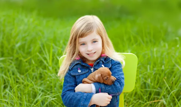Sarışın çocuk kızla yeşil çim içinde evde beslenen hayvan köpek yavrusu — Stok fotoğraf