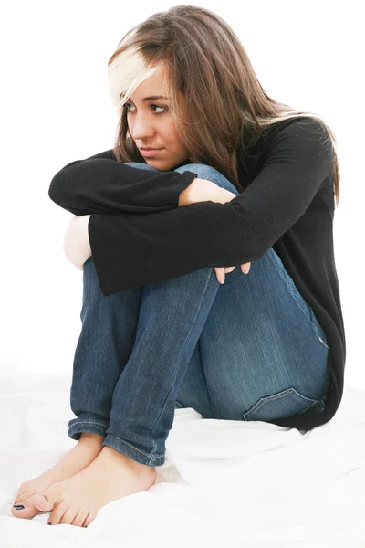 Chica triste adolescente se sienta brazos entrelazados alrededor de las piernas. Aislado en un... — Foto de Stock