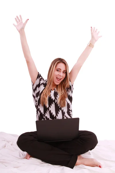 Woman sitting on the bed with a laptop computer and arms up - is — Stock Photo, Image
