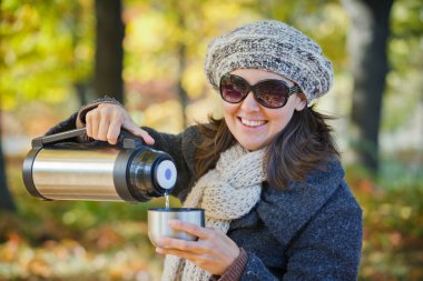 Woman drinks tea in autumn park clipart