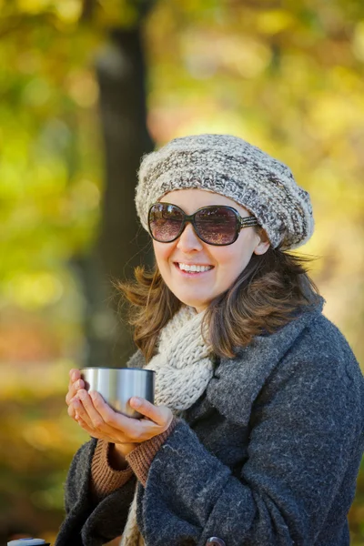 Woman drinks tea in autumn park