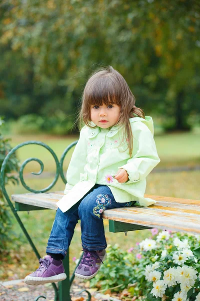 Маленькая девочка сидит на скамейке в парке — стоковое фото