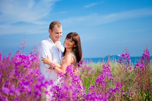 Romantisch paar onder paarse bloemen in de buurt van blauwe zee — Stockfoto