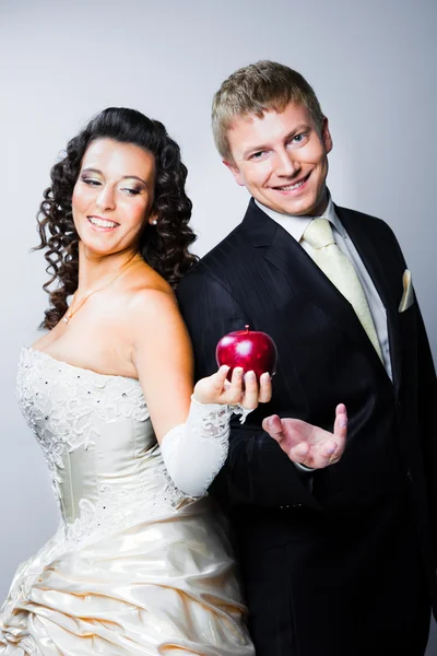 Frisch verheiratete Braut verführt lächelnden Bräutigam durch roten Apfel — Stockfoto