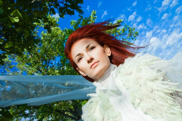 Beautiful woman in white against blue sky and green trees — Stock Photo, Image