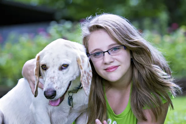 Schöne blonde Teenager umarmt weißen Hund im Freien Stockfoto