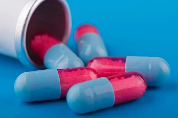 Cápsulas (pílulas) são azuis e vermelhas espalhadas em um fundo azul — Fotografia de Stock