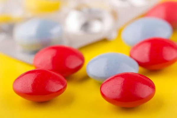 Pillole rosse e blu sdraiate su un tavolo giallo — Foto Stock