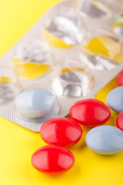 Pillole rosse e blu sdraiate su un tavolo giallo — Foto Stock