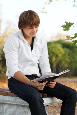 Young relaxed man reading book in nature, autumn clipart