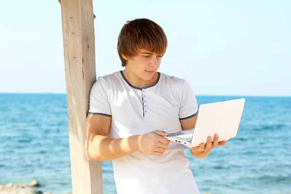 Młody człowiek korzysta z laptopa na plaży — Zdjęcie stockowe