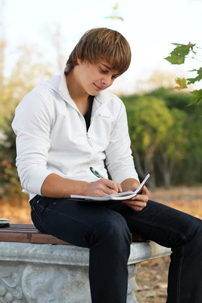 Χαρούμενος νεαρός γράψτε στο σημειωματάριο, φθινόπωρο σε εξωτερικούς χώρους — Φωτογραφία Αρχείου