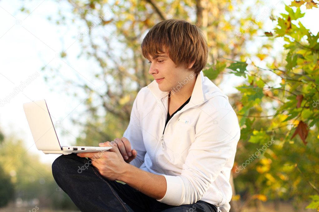 Young Man sitting in a bench with a laptop computer, autumn