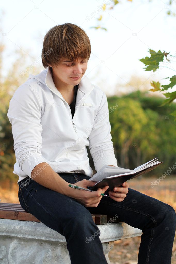 Young relaxed man reading book in nature, autumn